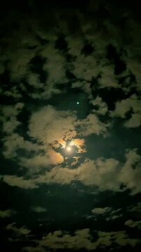 A celestial orb shines dimly through a thick blanket of swirling clouds, creating an eerie yet beautiful nocturnal scene in the dark sky.
