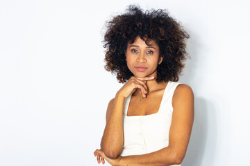 Confident young black woman with natural afro hair posing against white background, thoughtful...