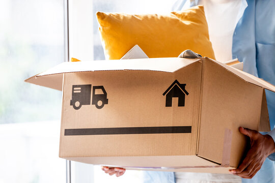 Man holding a cardboard box with moving symbols. Concept of moving, new home, and residential relocation. Bright and modern background