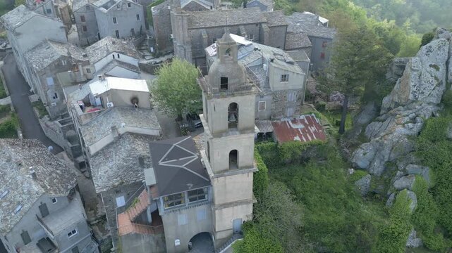 Drone orbiting historic church bell tower of Loreto di Casinca under cloudy sky, Corsica, France