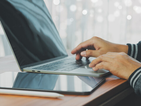 Person typing on laptop keyboard at wooden desk with tablet and stylus nearby, focused modern remote work scene conveying productivity and calm