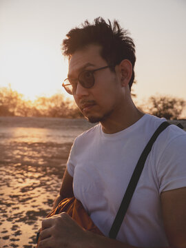 Thoughtful individual stands on coast capturing sunset moments with camera