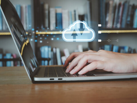 Person typing on laptop keyboard with cloud upload download icon overlay symbolizing data sync and remote storage in cozy library workspace, productive and connected