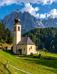 Fototapeta premium Idyllic alpine church nestled in a vibrant green meadow against majestic peaks