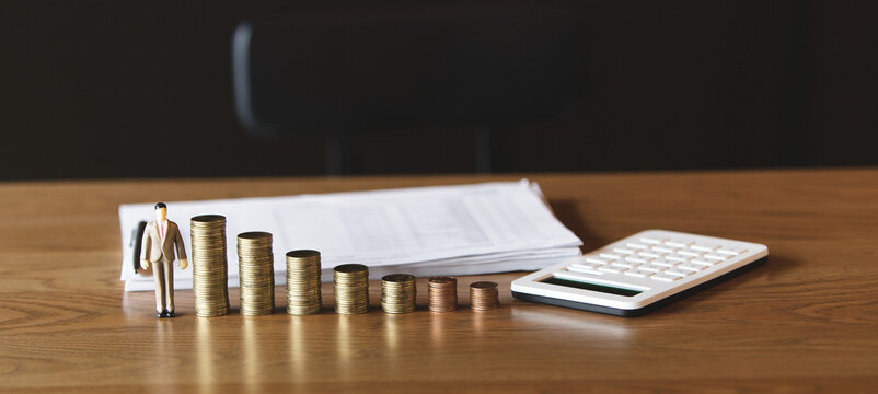 Stacked coins with a miniature businessman and calculator on a wooden desk, symbolizing financial growth, investment planning, and business success