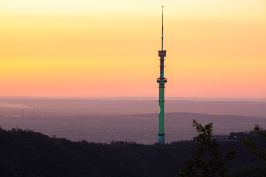 Almaty TV Tower on Kok Tobe hill at sunset. Iconic landmark and mountain silhouette against dramatic evening sky in Kazakhstan.