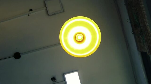 Bright yellow-orange ceiling light fixture glowing intensely, casting warm, energetic illumination in a room