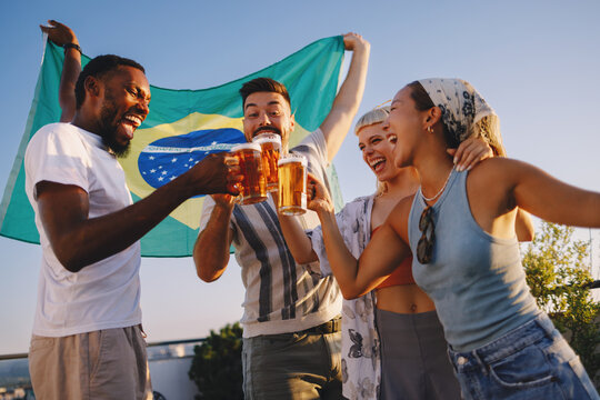 Group of diverse friends cheering with beer and waving the brazil flag at an outdoor party