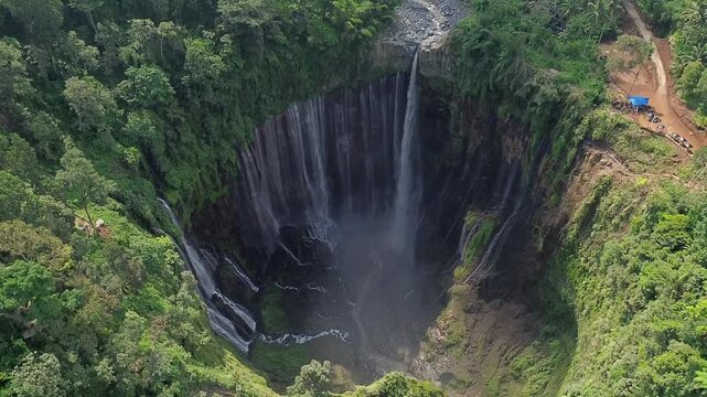 Beautiful cinematic footage of Coban Sewu or Tumpak Sewu Waterfall, a famous landmark in Lumajang, Indonesia. Wide shot of thousand waterfalls surrounded by dense green forest and tropical plants.