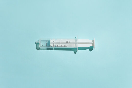 Sterile plastic syringe without a needle in a minimalist flat lay composition. The medical tool casts a sharp shadow on a clean pastel blue background. Clean, clinical aesthetic