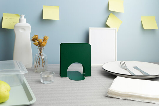 Contemporary still life of household items, dish soap, and tableware against a blue wall with sticky notes