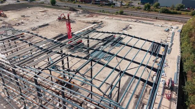 Construction of new building structure takes place in industrial area with cranes and machinery involved