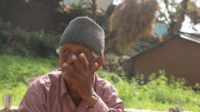 Portrait of an elderly man sitting outside his home in a rural mountain village in India, reflecting simple living, aging, and poverty in a natural countryside environment.