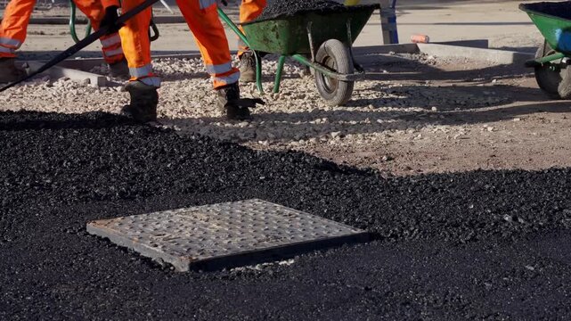 Workers lay asphalt on a construction site while surrounding area is prepared for paving during daytime hours