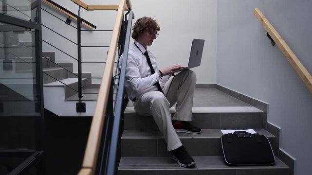 Employee secretly playing games on laptop during work break hiding on office stairs avoiding duties procrastination behavior casual distraction unproductive moment workplace reality