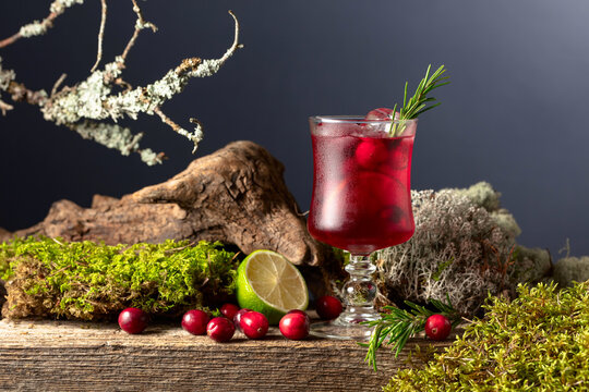 Cranberry cocktail with ice, lime, and rosemary on a old wooden board.