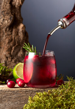 Cranberry cocktail with ice, lime, and rosemary on a old wooden board.