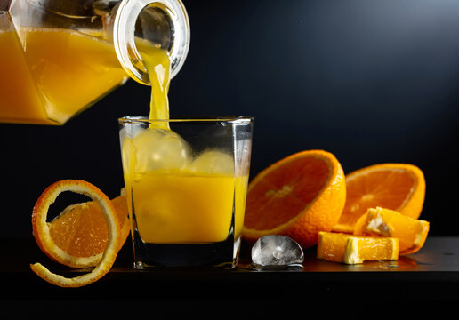 Glass of orange juice with ice on a black background.