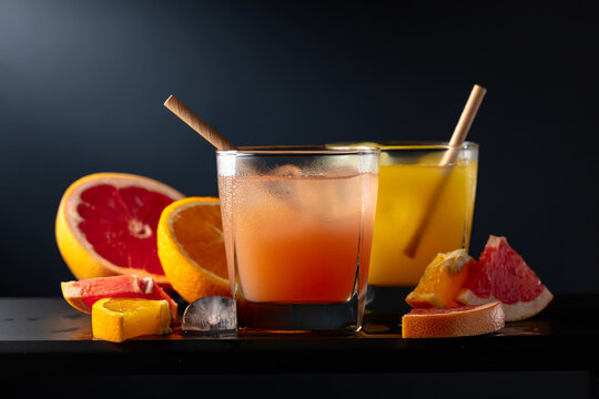 Glasses of grapefruit and orange juice with ice on a black background.