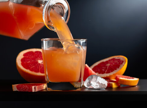 Glass of grapefruit juice with ice on a black background.