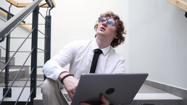 Young man with laptop works on stairs focused on tasks thinking about solutions modern remote work lifestyle productivity concentration casual workspace daily routine