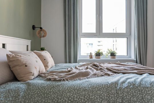 Interior of a bedroom in cozy apartment with window. Comfortable bed with pillow and boho style. Relax and sleep. Real estate.