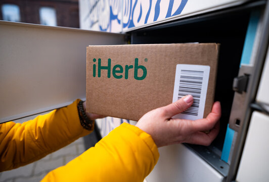 Poznan, Poland - 31 December 2025: Girl Picking Up A Delivered Cardboard Box From An Online Store Iherb At An Automated Parcel Locker