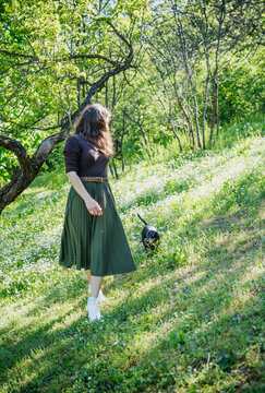 Happy young woman walking with her black dachshund dog on a green lawn in a park
