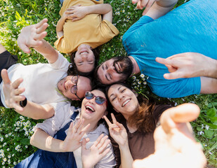 Fototapeta premium Five happy adult friends lying in a circle head to head on grass waving at camera