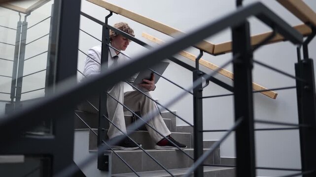 Tired office worker sitting on stairs working on laptop after work feeling exhausted and low energy continuing tasks despite fatigue and long day showing burnout and effort