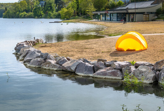 Orange wind shelter tent on the lakeshore on a sunny day in France.