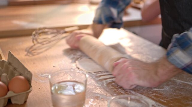 Close-up hands of a chef using a rolling pin to make cookies, with sunlight shining in the background on a morning