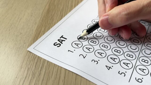 Hand filling correct answers on multiple choice test sheet. Concept of exam preparation, answer checking and student assessment