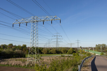 Fototapeta premium High voltage power transmission towers along rural road – electricity grid infrastructure in countryside landscape