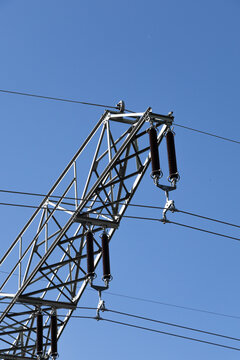 High voltage transmission tower detail with insulators and power lines against blue sky