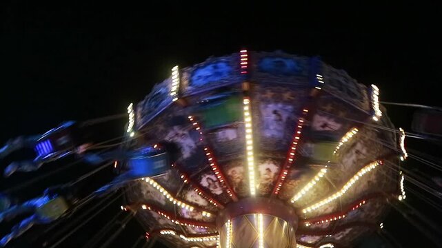 Brightly lit carousel ride spinning at night with motion blur, creating a vibrant and dynamic scene at an amusement park.