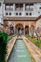 Obraz premium Generalife garden at the Alhambra with a long rectangular water channel and small spraying fountains leading to an ornate Moorish palace amid hedges and historic architecture