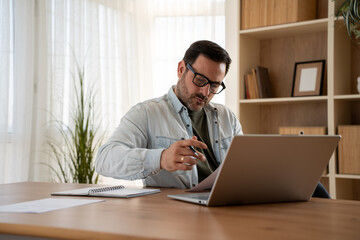 Fototapeta premium Focused male professional working remotely on laptop at home desk