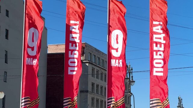 Red flags with text in Russian celebrating Victory Day on 9 May. Outdoor street decoration for memorial event. Banner with military ribbon symbol in urban city environment. Russia holiday.