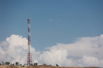 Obraz premium Red and white telecommunications tower on a hill against a blue sky with fluffy clouds