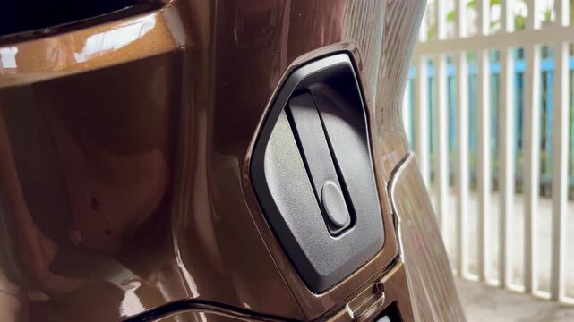 An Asian woman is closing the luggage hook located on the front deck of an automatic motorbike, using a hook made of plastic.
