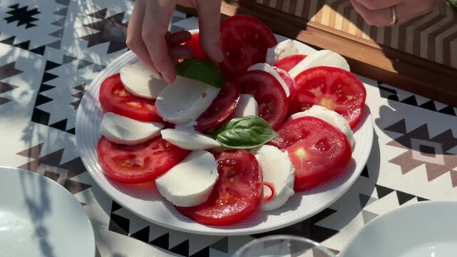 Fresh caprese salad on patterned table, sliced tomatoes mozzarella and basil arranged on white plate, bright summer light for healthy italian dining