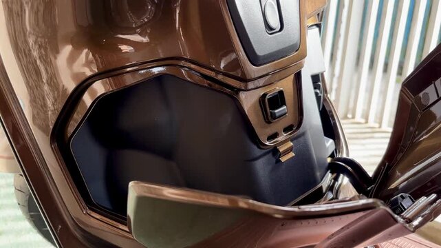 A video featuring an Asian woman opening the storage compartment of a brown scooter, demonstrating its practical design, internal space, and everyday usability for urban transportation.