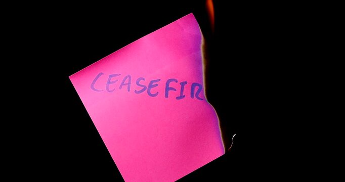 Pink post it note with ceasefire text burning on black background symbolizing the end of peace and the start of war and conflict now.