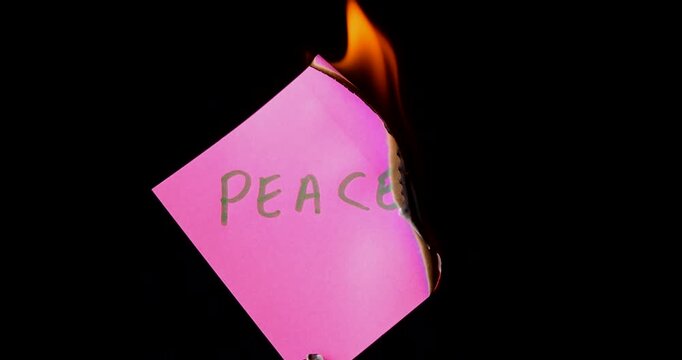 Pink post it note with peace text burning on black background symbolizing the end of harmony and the start of war and destruction.