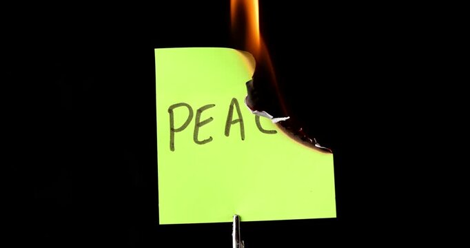 Yellow post it note with peace text burning on black background symbolizing the end of harmony and the start of war and destruction.