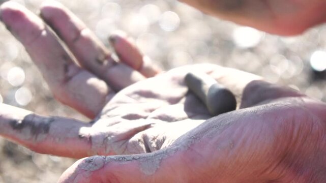 Hands clay crafting, person shaping gray clay into a small cat figurine on a sunny day outdoors