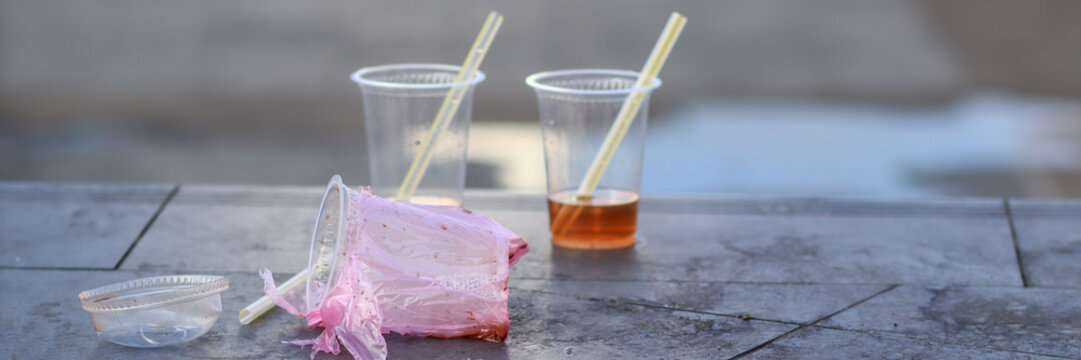Abandoned plastic cups with straws and plastic wrapper left on outdoor stone surface representing single use plastic waste and urban littering problem