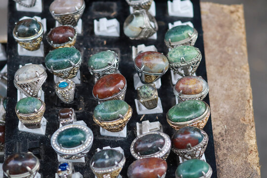 Variety of colorful natural gemstone silver rings arranged in rows on display board at traditional market in Indonesia