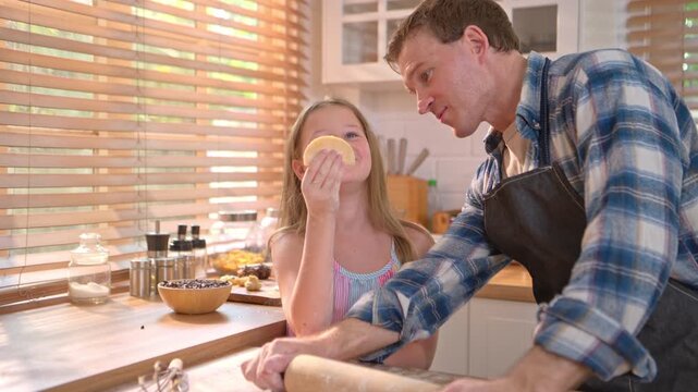 Little girl shaping dough in kitchen with father nearby, representing learning, creativity, and childhood home cooking experience